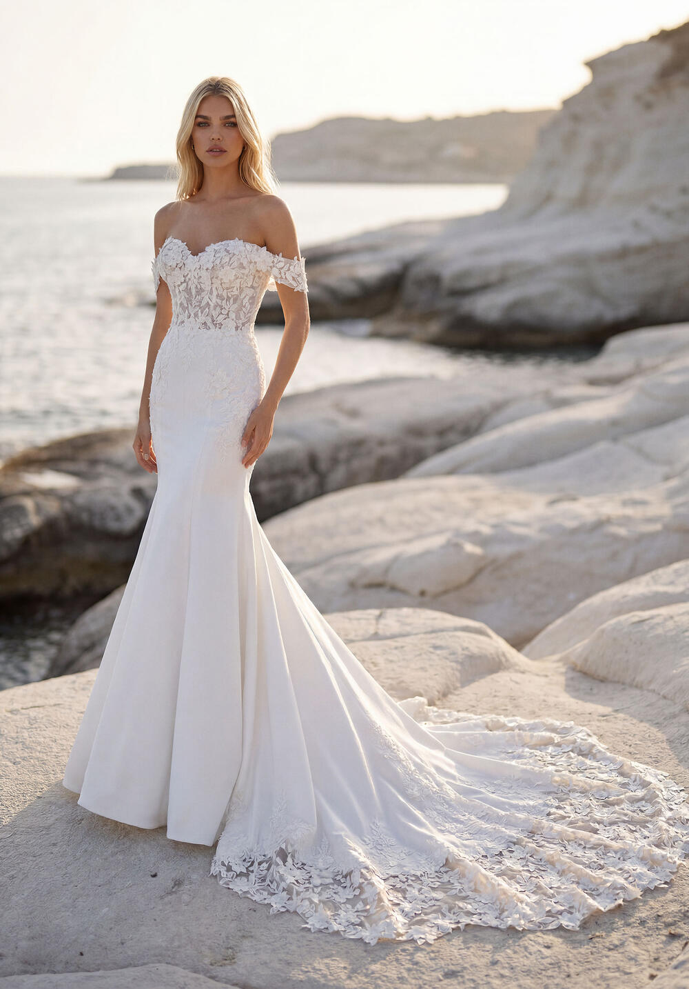 Morilee off-the-shoulder fit and flare gown with a lace-trimmed train on seaside rocks