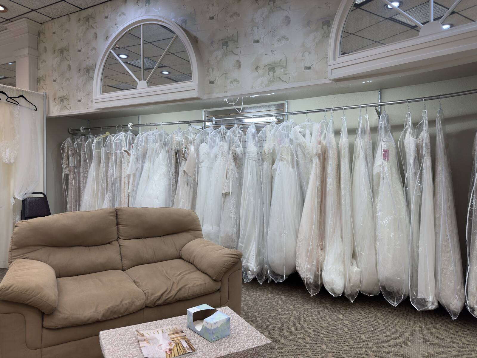 Bridal salon seating area beside racks of wedding gowns